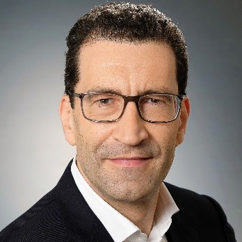 Reinhard German im Anzug mit Brille und kurzen schwarzen Haaren.