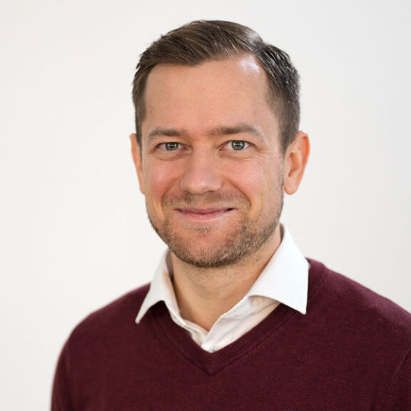 Bastian Ritter im roten Pullover über weißem Hemd.