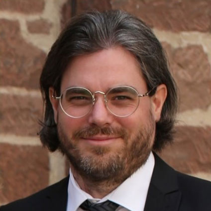 Tobias Knorsch mit Brille, Anzug und langen schwarzen Haaren.